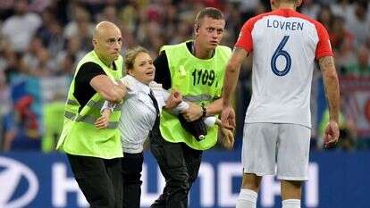 המאבטחים גוררים את חברת הלהקה מחוץ למגרש. לוברן מתצפת. | EPA המאבטחים גוררים את חברת הלהקה מחוץ למגרש. לוברן מתצפת. | EPA