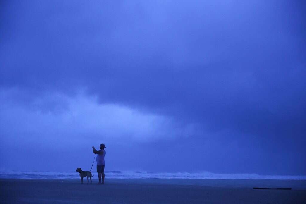 אדם מטייל עם כלבו על החוף המעונן בקרוליינה. | AFP