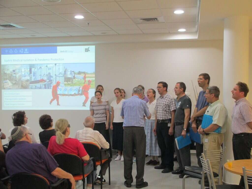 סגנון מאופק ומיושן בתוך נוף תעשייתי. עובדי המפעל שרים פסוקי נביאים בפני המסיירים. | ד"ר אבישי טייכר, מתוך אתר פיקיוויקי