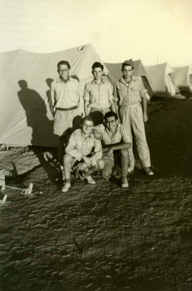 יהודה נוימן (עומד במרכז) עם חלק מהשבויים במחנה אום אל ג'מאל, ירדן 1948. | מתוך אוסף יהודה נוימן המוקדש ללוחמי גוש עציון. זוהה ותוארך ע"י רוני קניגסברג. באדיבות המשפחה