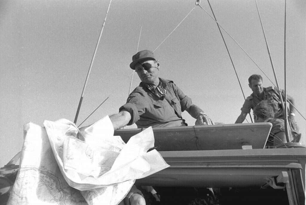 שר הביטחון משה דיין על נגמ"ש, מעביר מפות בביקור בצד המעברי של תעלת סואץ. 20.10.1973. | במחנה. באדיבות ארכיון צה״ל במשרד הביטחון