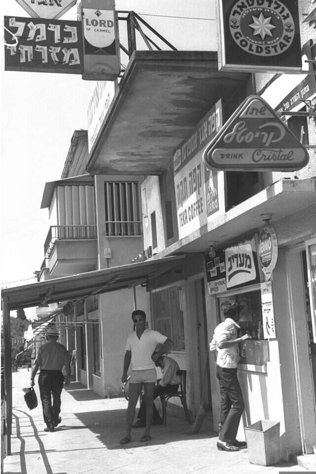 על הדרך הראשית עמדו בתי קפה, חנויות נעליים, חנות מקררים, מספרה. הוד־השרון, 1971. | משה מילנר, לע"מ