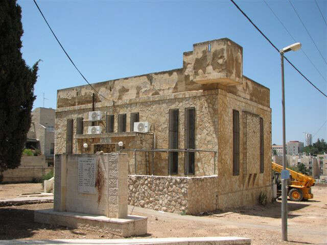 בית הכנסת בשכונת מקור חיים שנבנה בשנת תרפ"ט, עם עמדות השמירה והאנדרטה בחזיתו. | מיכאל יעקובסון