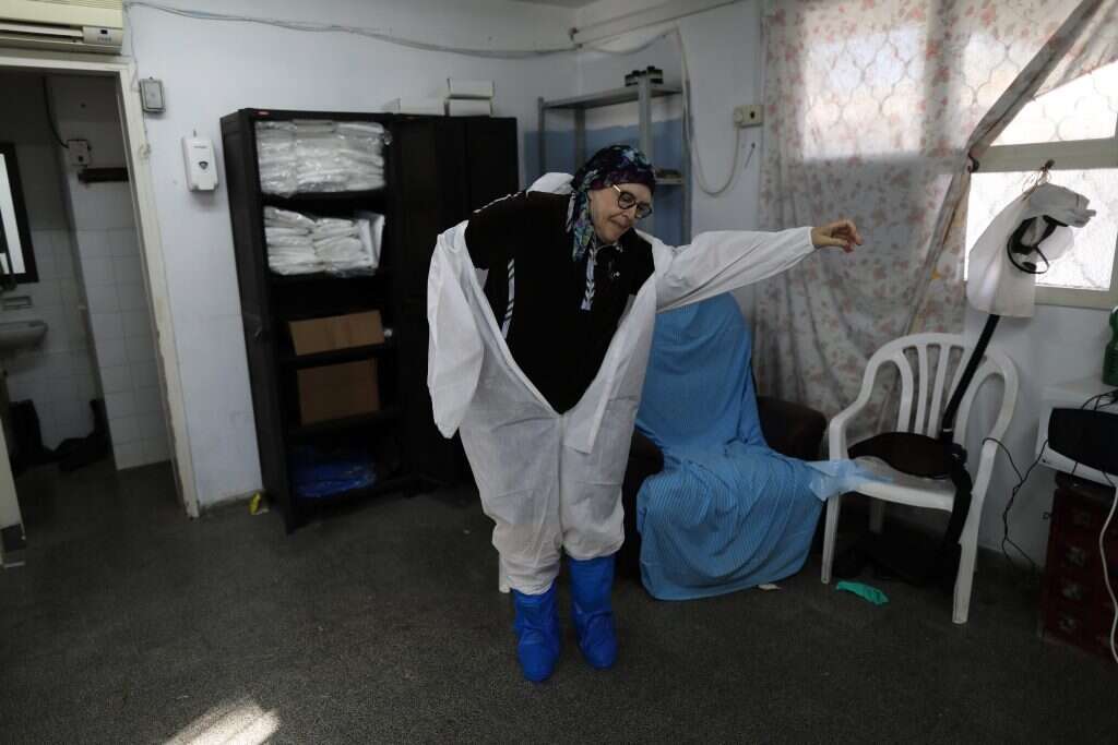 גלגלי השיניים מאחורי המחוג. עובדת לובשת ציוד מגן במתקן חברה קדישא בחולון. | EPA