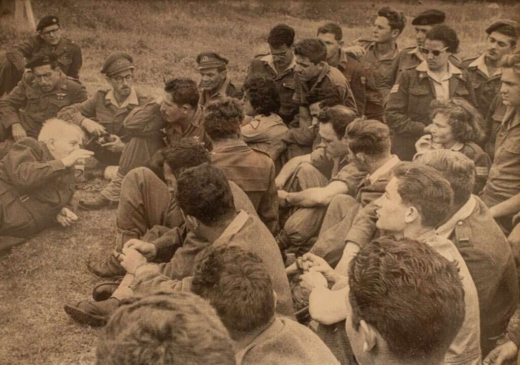 בן־גוריון (משמאל) במפגש עם חניכים בקורס מתקדם להכשרת סרנים וותיקים, 1950. מאחורי ב"ג נראים מפקד הקורס ולימים הרמטכ"ל חיים לסקוב (למעלה בתמונה), ומתחתיו רחבעם זאבי. עמי צור מימין עם הכובע. | באדיבות עמי צור