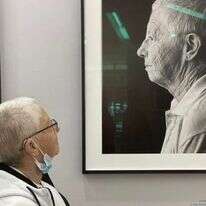 ריטה ארד מביטה בתמונתה המוצגת בתערוכה. | נעם בן־גוריון מוסרי