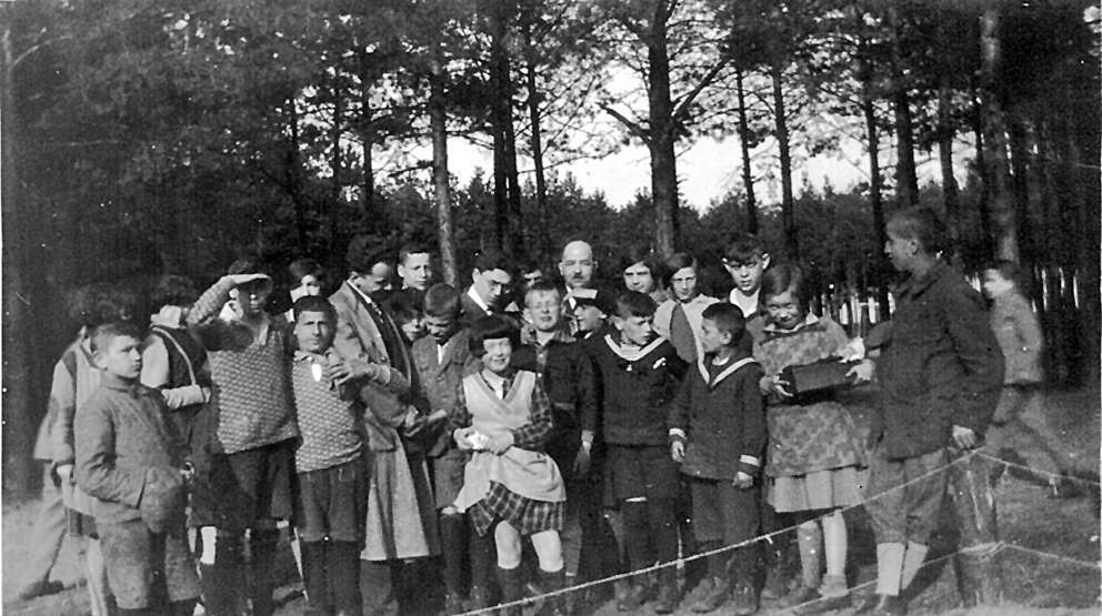 ארתור פיינר, יהודי בן תשעים מניו־יורק, סיפר שעבד בכפר הילדים ונהג לצלם את חיי היומיום. סאלי (קירח, מאחור) עם הילדים. | ארתור פיינר והמחלקה לזכר השואה בתוך ההסתדרות הציונית העולמית, באדיבות החוקרים רוני דותן, טטיאנה מתניה רוגה והבמאי דן וולמן