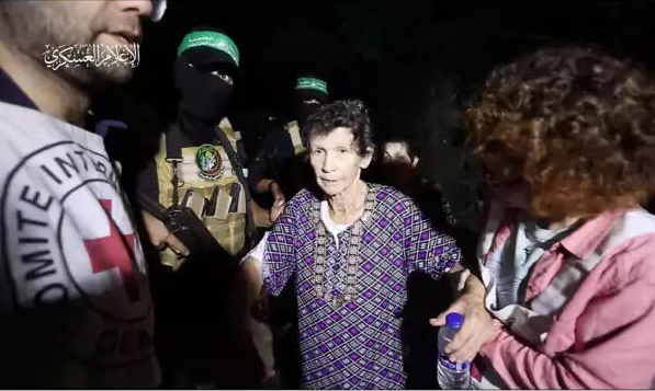 יוכבד ליפשיץ מקיבוץ ניר־עוז עם שחרורה משבי חמאס, כשמחבלי הארגון ברקע. | מתוך הרשתות החברתיות לפי סעיף 27 א' לחוק זכויות יוצרים