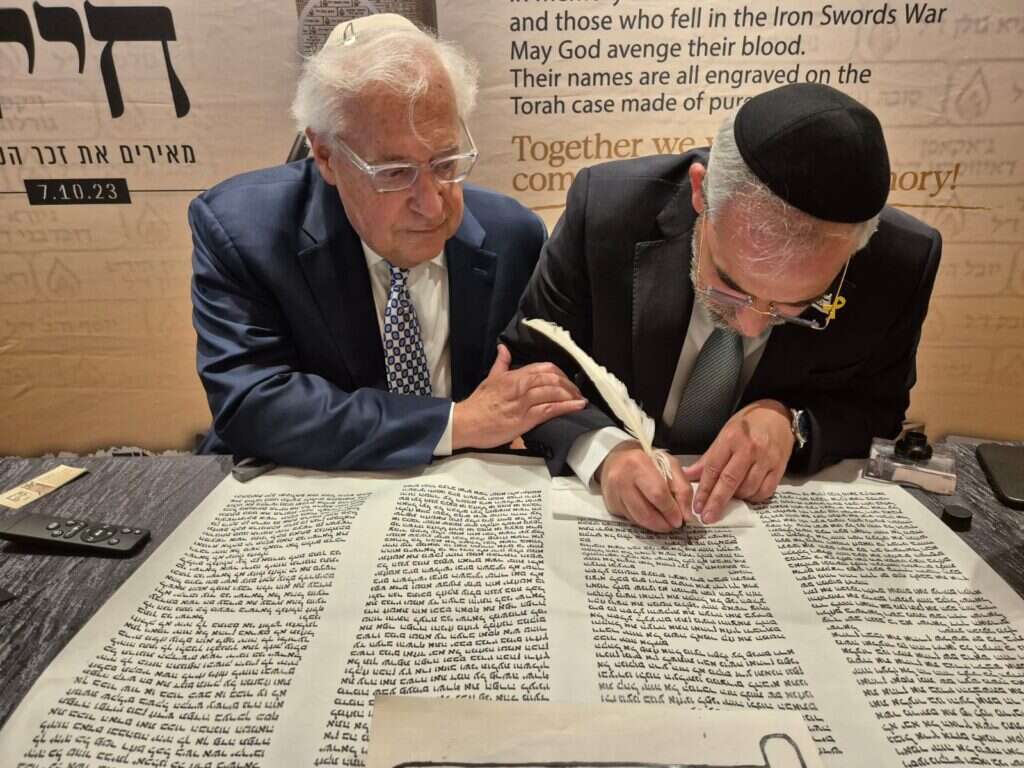 השגריר לשעבר פרידמן כותב אות בספר התורה לזכר חללי חרבות ברזל שהוצג בוועידת "בשבע" בניו יורק. | מיכאל טוכפלד