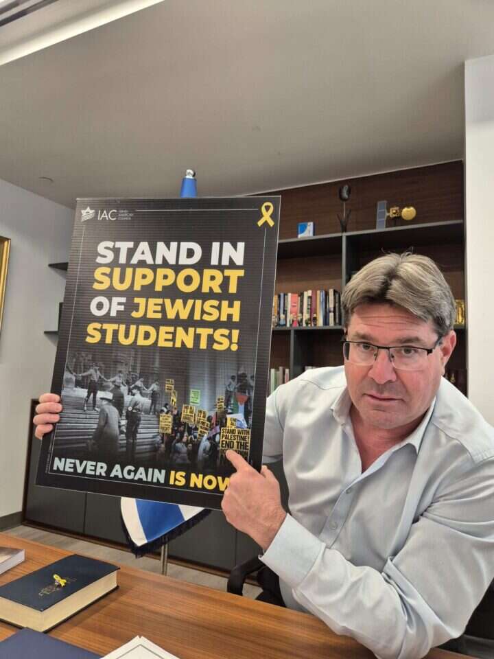 אקוניס, במשרדו בניו־יורק השבוע, מציג כרזה המראה פעילות נגד סטודנטים יהודים בשנת 1933 והיום. | מיכאל טוכפלד