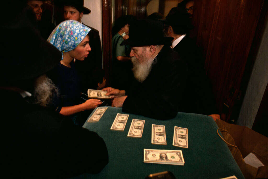 הרבי מלובביץ' מחלק שטרות דולר לאנשי החסידות ב־1991. | גטי אימג'ס