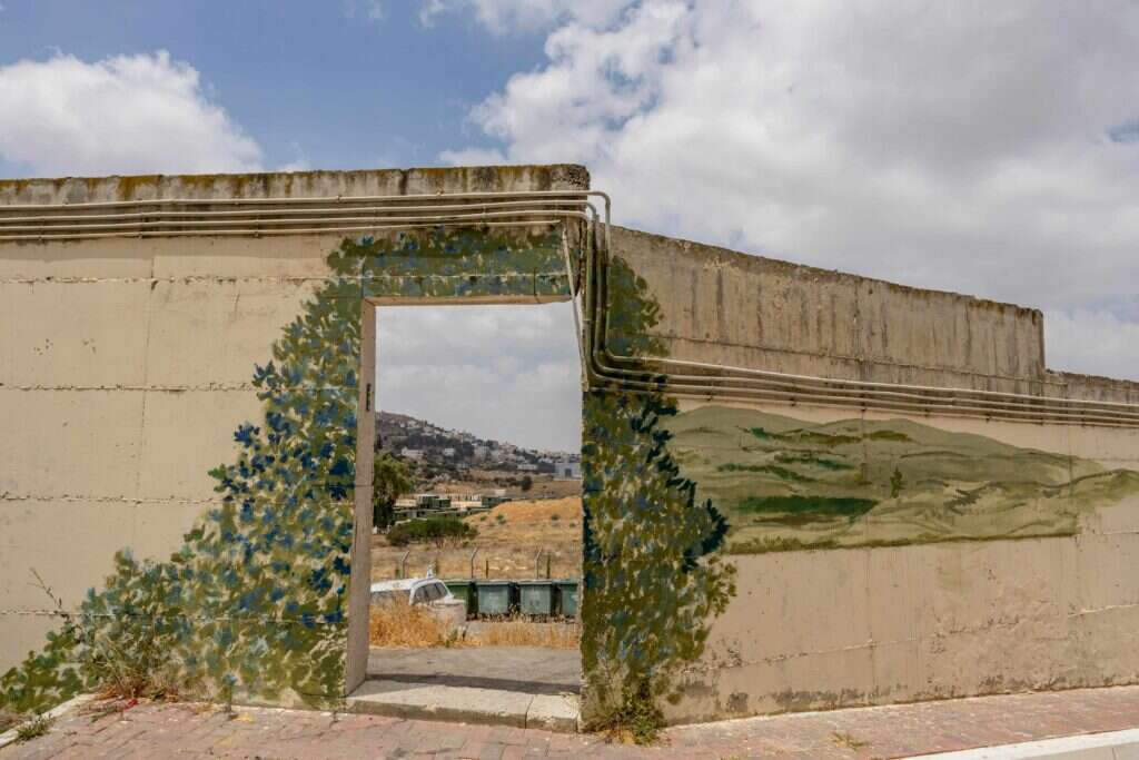 החומה שמקיפה את המקום כוסתה בציורים, לטשטש את נוכחותה. | נעמה שטרן
