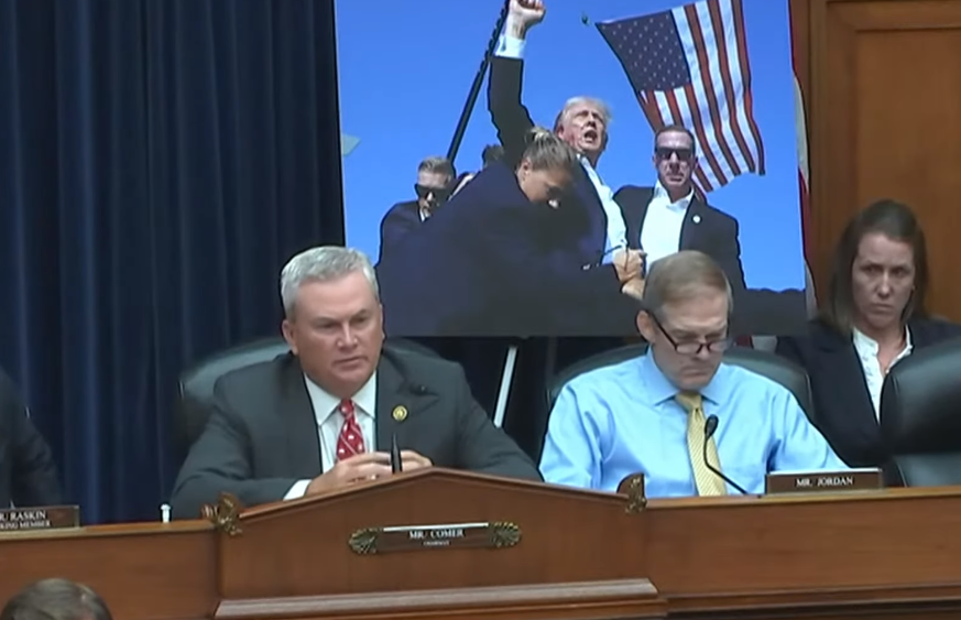 ראש הוועדה, ג'יימס קומר, וברקע התמונה האייקונית של טראמפ