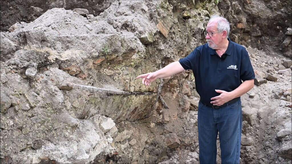 דר' ג'ון זליגמן מרשות העתיקות מצביע על עמוד הענק שהיה חלק מהמראה האייקוני של בית הכנסת. | רשות העתיקות