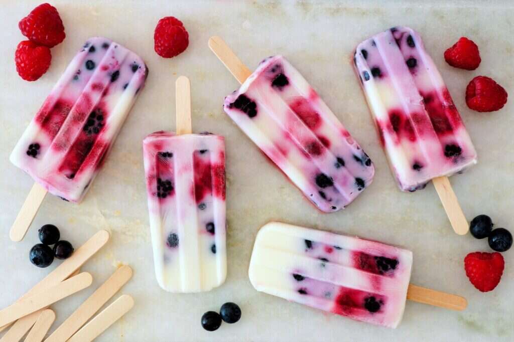 Healthy mixed berry yogurt popsicles with fruit on a white marble background