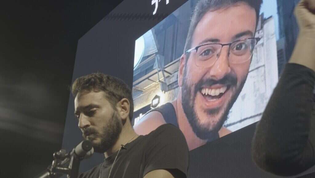 יונתן שמריז, אחיו של החטוף אלון שמריז הי"ד, על רקע תמונת אחיו. | עמרי קורן יונתן שמריז, אחיו של החטוף אלון שמריז הי"ד, על רקע תמונת אחיו. | עמרי קורן