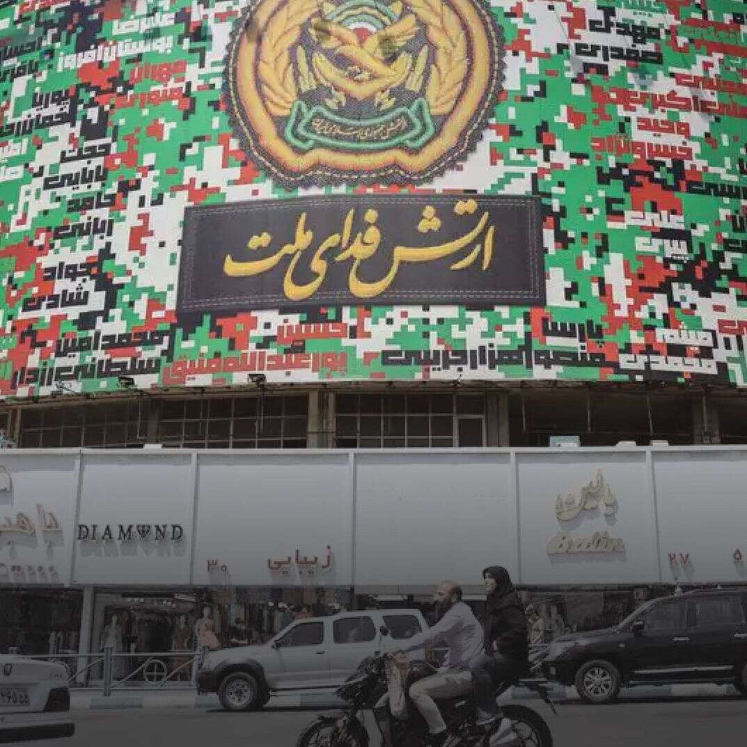 איראנים חולפים על פני פוסטר ענק בצבעי דגל איראן ועליו כתוב בפרסית "הצבא מקריב את עצמו למען האומה" בכיכר ואליאסר בטהרן, איראן | EPA