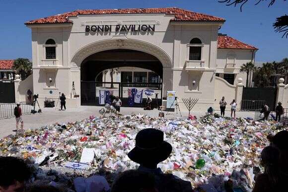 אבלים עומדים ליד אנדרטאות המוערמות בחזית ביתן בונדי, לזכר קורבנות הירי בחוף בונדי, בסידני ב-17 בדצמבר 2025 | דיוויד גריי / AFP אבלים עומדים ליד אנדרטאות המוערמות בחזית ביתן בונדי, לזכר קורבנות הירי בחוף בונדי, בסידני ב-17 בדצמבר 2025 | דיוויד גריי / AFP