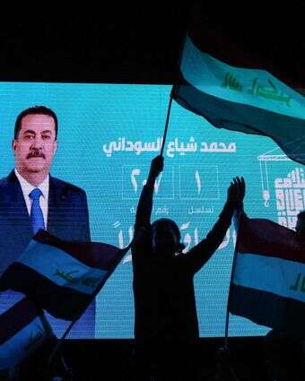 תומכיו של ראש ממשלת עיראק המכהן, מוחמד שיעה אל-סודאני, מנופפים בדגלי המדינה מול מסך המציג את דיוקנו וחוגגים לאחר פרסום תוצאות הבחירות הראשוניות בבגדד | אחמד אל-רוביי / AFP