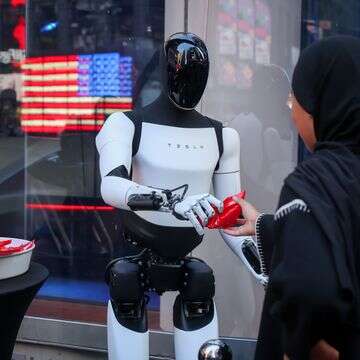 רובוט של טסלה אופטימוס מחלק ממתקים מול בורסת נאסד"ק בניו יורק | מייקל נגל/בלומברג רובוט של טסלה אופטימוס מחלק ממתקים מול בורסת נאסד"ק בניו יורק | מייקל נגל/בלומברג