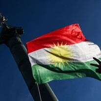 מפגין מניף את סמל השלום באצבעותיו מול דגל כורדיסטן במהלך הפגנת סולידריות עם הכורדים בצפון סוריה | בלנקה קרוז / AFP