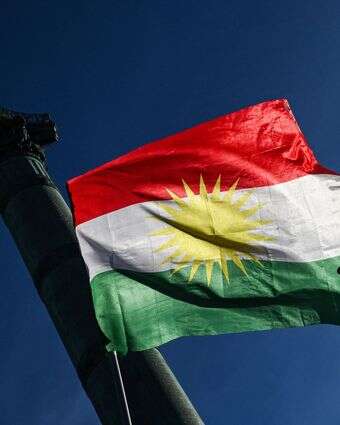 מפגין מניף את סמל השלום באצבעותיו מול דגל כורדיסטן במהלך הפגנת סולידריות עם הכורדים בצפון סוריה | בלנקה קרוז / AFP