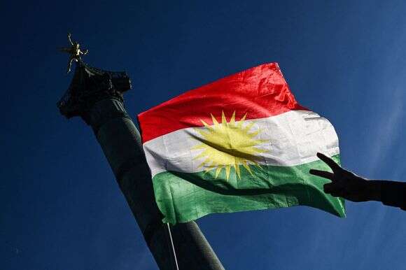 מפגין מניף את סמל השלום באצבעותיו מול דגל כורדיסטן במהלך הפגנת סולידריות עם הכורדים בצפון סוריה | בלנקה קרוז / AFP