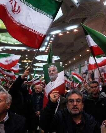 אנשים מנופפים בדגלי איראן בעוד אחד מהם מרים פוסטר של מפקד כוח קודס של משמרות המהפכה האיראניים, הגנרל קאסם סולימאני | AP/Vahid Salemi