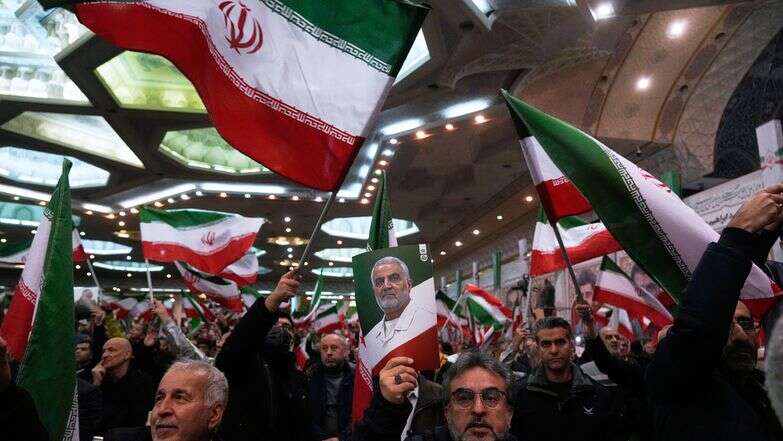 אנשים מנופפים בדגלי איראן בעוד אחד מהם מרים פוסטר של מפקד כוח קודס של משמרות המהפכה האיראניים, הגנרל קאסם סולימאני | AP/Vahid Salemi