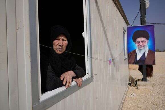 סוריה אל-חסן, בת 75, אישה שיעית סורית, מביטה מחלון יחידת הדיור שלה ליד דיוקן של המנהיג העליון של איראן, האייתוללה עלי חמינאי, במתחם הדיור על שם האימאם עלי, שם מתגוררים מאות מוסלמים שיעים | AP/חוסיין מאלה