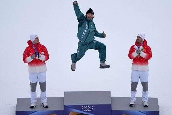 לוקאס פיניירו בראתן הברזילאי, במרכז, מנצח מרוץ סלאלום ענק לגברים בסקי אלפיני, קופץ בחגיגה על הפודיום לצד מרקו אודרמט משווhיץ, שסיים במקום השני, ולואיק מילארד משווhיץ, שסיים במקום השלישי, באולימפיאדת החורף 2026 | AP