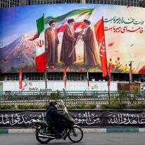 גבר רוכב על אופנוע ועובר ליד שלט המוצג בכיכר ואליאסר במרכז טהרן | AFP