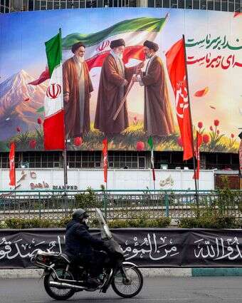 גבר רוכב על אופנוע ועובר ליד שלט המוצג בכיכר ואליאסר במרכז טהרן | AFP