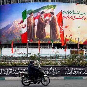 גבר רוכב על אופנוע ועובר ליד שלט המוצג בכיכר ואליאסר במרכז טהרן | AFP