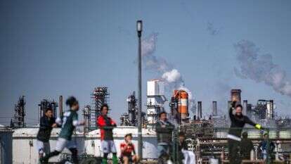 – אנשים משחקים כדורגל בפארק היגאשי-אוגישימה היגאשי, כאשר נראים מיכלי אחסון אנרגיה ליד בית זיקוק לנפט באזור התעשייה קייהין, חגורה תעשייתית מרכזית במפרץ טוקיו | פיליפ פונג / AFP