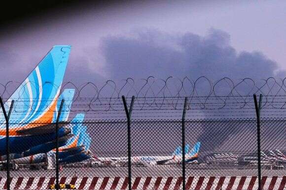 מטוס של FlyDubai חונה בנמל התעופה הבינלאומי של דובאי כאשר עשן עולה ברקע לאחר שרחפן פגע במיכל דלק מוקדם בבוקר, מה שאילץ את ההשעיה הזמנית של טיסות, בדובאי, איחוד האמירויות הערביות | AP