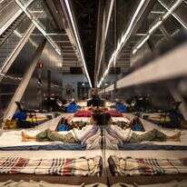 אישה משתמשת בטלפון נייד כשהיא שוכבת על מזרן בתחנת רכבת ששימשה כמקלט תת-קרקעי | אולימפיה דה מייסמונט / AFP