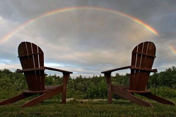 שני כיסאות אדירונדק ריקים ליד בור אש, קשת בענן נמתחת על פני השמיים באדמס פונד באיסט דרי, ניו המפשייר | AP/צ'ארלס קרופה