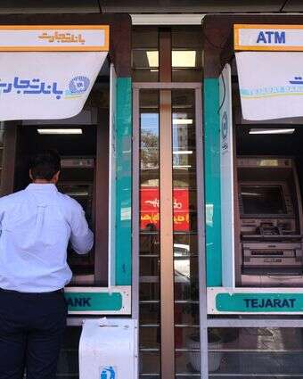 אדם מושך מזומן מכספומט בבנק בטהרן, מאי 26' | AFP אדם מושך מזומן מכספומט בבנק בטהרן, מאי 26' | AFP
