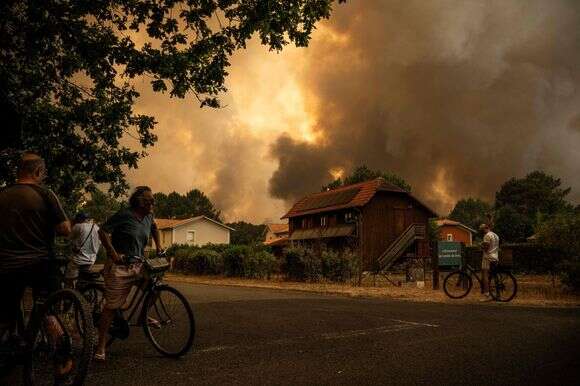 אחת משרפות הענק בצרפת, יולי 26 | (FILES) Residents on their bicycle look at smoke rising behind a residential area during a wildfire near Lege-Cap-Ferret, southwestern France on July 23, 2026. France has been battered by three heatwaves since May as part of increasingly common extreme weather episodes linked to climate change, causing thousands of excess deaths and fuelling wildfires. (Photo by JULIEN DE ROSA / AFP)