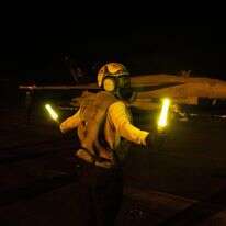 מלח בצי האמריקני המכווין מטוס F/A-18E Super Hornet על סיפון הטיסה של נושאת המטוסים מסדרת "נימיץ", ה-USS George H.W. Bush | various sources / AFP) / RESTRICTED TO EDITORIAL USE - MANDATORY CREDIT "AFP PHOTO / US NAVY / NAVCENT PUBLIC AFFAIRS