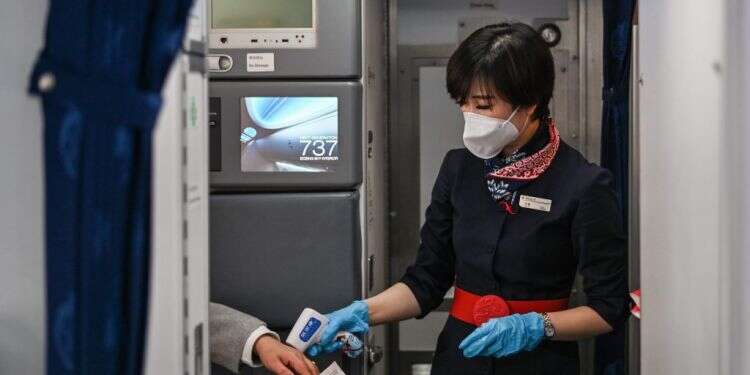 דיילת בודקת חום לנוסע בשדה התעופה בוואהן, סין. פברואר 2021. צילום: AFP מומחים: נעטה מסכות בטיסה גם לאחר המגפה