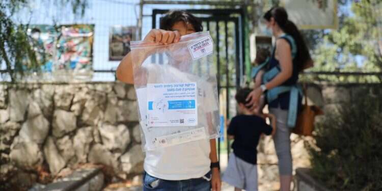 תלמיד מחזיק בדיקת קורונה מחוץ לבית ספר בירושלים. צילום: EPA בצל השיא במאומתים ליום: נפתחה שנת הלימודים בישראל