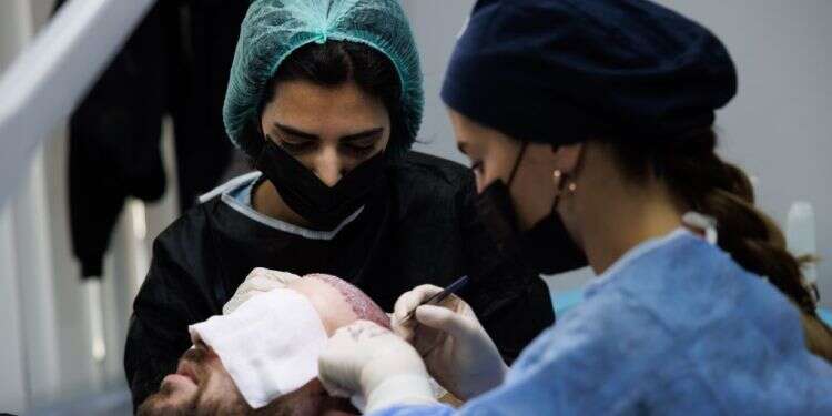 מאור בעת ביצוע ההשתלה. למטה: מסדרון מרפאת Hair Center Of Turkey שבאיסטנבול. צילום: אנצ'ו גוש, ג'יני מסע שורשים: איך הפכה טורקיה למעצמה עולמית בתחום השתלת השיער