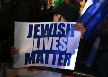 אישה מחזיקה שלט עם הכיתוב "חיי יהודים נחשבים" בהפגנה נגד אנטישמיות בתפוצות