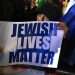 אישה מחזיקה שלט עם הכיתוב "חיי יהודים נחשבים" בהפגנה נגד אנטישמיות בתפוצות