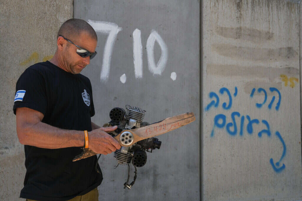 "לפני כשלושה חודשים נפל כאן חלק של כטב"ם, ורועי אטלי נפצע באורח קשה. "הייתה התרעה ארבעים דקות לפני כן, בשלב מסוים חזרנו לשגרה, ואחרי שמונה דקות נפל הכטב"ם", מספרים החברים. "לפעמים יש אזעקה, ולפעמים אתה פשוט שומע מכסחת דשא שעפה באוויר, וצריך למצוא מחסה תוך כמה שניות" בתמונה: ארז אדר רבש״צ הקיבוץ עם מנוע של כטב״מ שפגע בקיבוץ. צילום: אייל מרגולין - ג׳יני