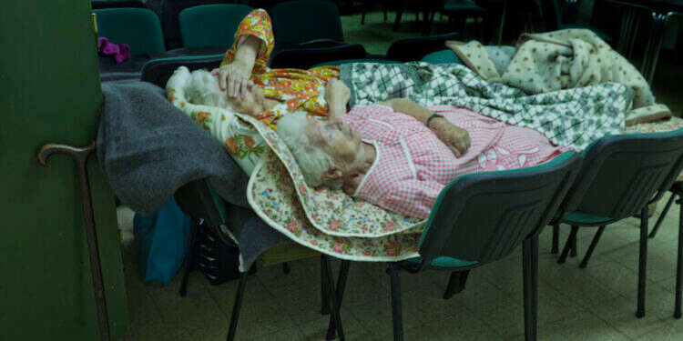 שתי אחיות )ניצולות שואה(, אחת מאשקלון ואחת מבאר שבע, ישנות על כיסאות במבנה ציבורי בזמן מבצע צוק איתן. רינה קסטלנובו, 2014