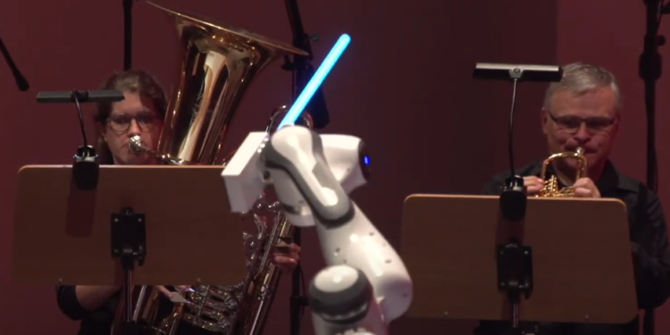 רובוט בעל שלוש זרועות מנצח על תזמורת באמצעות חרבות אור